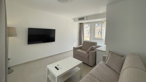 Un salon moderne avec un téléviseur à écran plat, un canapé, un fauteuil et une petite table.