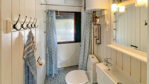 Ein kleines Badezimmer mit Toilette, Waschbecken und Dusche. Handtuchhalter und Fenster mit Vorhang sind vorhanden.