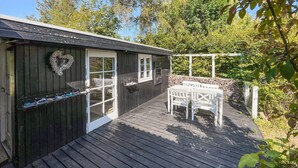 Eine Holzterrasse mit einem weißen Tisch und Stühlen, einer herzförmigen Dekoration und einer Steinmauer.