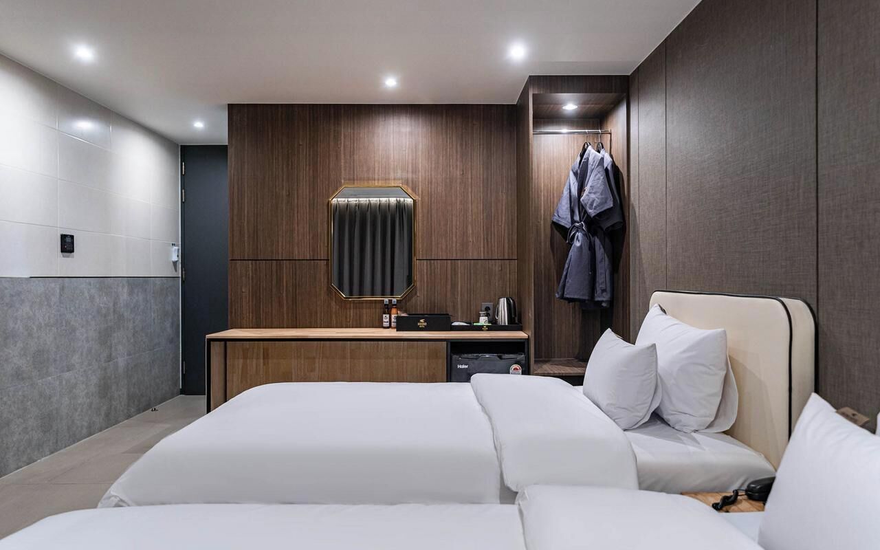 A modern hotel room with a large bed, a bedside table, a mirror, and a wardrobe.