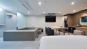 A modern hotel room with a large bed, a bathtub, a dining area with chairs, a TV mounted on the wall, and a wooden vanity with a mirror. - Suwon Hound Hotel (Suwon)