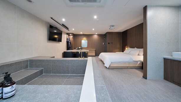 A modern hotel room with a large bed, a separate seating area, a built-in TV, and a small bathroom. - Suwon Hound Hotel (Suwon)