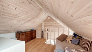 A cozy attic bedroom with wooden walls and a sloped ceiling. It features a white bed, a wooden dresser, and a small kitchenette. - 1 bedroom beautiful apartment in Vallåkra (Vallåkra)