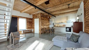 A spacious living area with a high ceiling and exposed wooden beams, a dining area with a wooden table and chairs, a kitchen with modern appliances, and a grey sofa with decorative pillows. - 1 bedroom beautiful apartment in Vallåkra (Vallåkra)