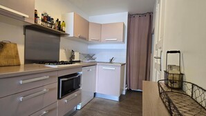 Une cuisine compacte équipée d’une cuisinière, d’un four, d’un four à micro-ondes et d’un lave-vaisselle. On y trouve une planche à découper en bois, un porte-épices et une étagère en métal avec des bocaux.