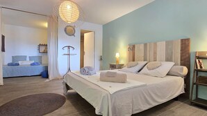 Une chambre à coucher comprenant un lit, des tables de chevet, un luminaire suspendu, un miroir et une porte donnant sur une autre pièce.