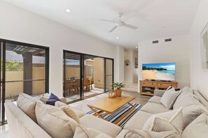 Ein modernes Wohnzimmer mit Sofa, Couchtisch und Fernseher, der eine Strandansicht zeigt.