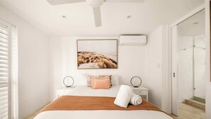 A modern bedroom with a large bed, a ceiling fan, a framed picture on the wall, and a bathroom door in the background. - Picture Perfect - Panoramic Views, Walk to Beach (Noosa Heads)
