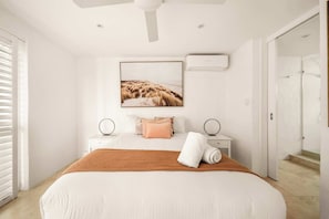 A modern bedroom with a large bed, a ceiling fan, a framed picture on the wall, and a bathroom door in the background. - Picture Perfect - Panoramic Views, Walk to Beach (Noosa Heads)