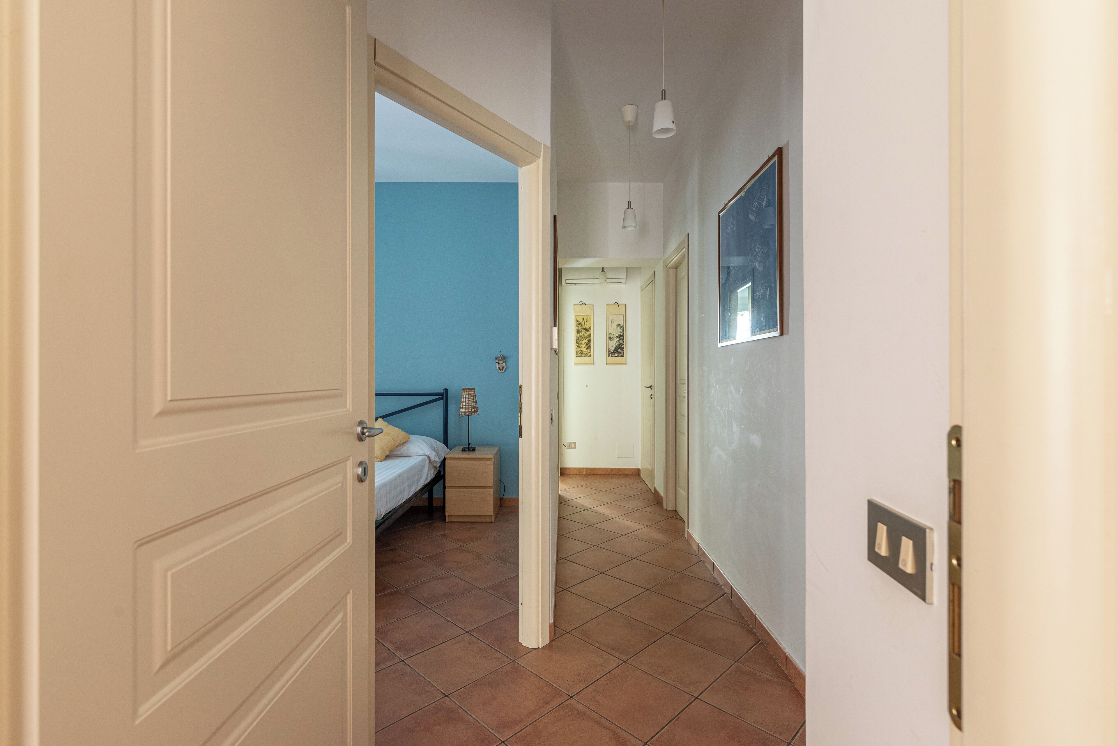 A hallway with a bed, bedside table, and wall-mounted lamp.