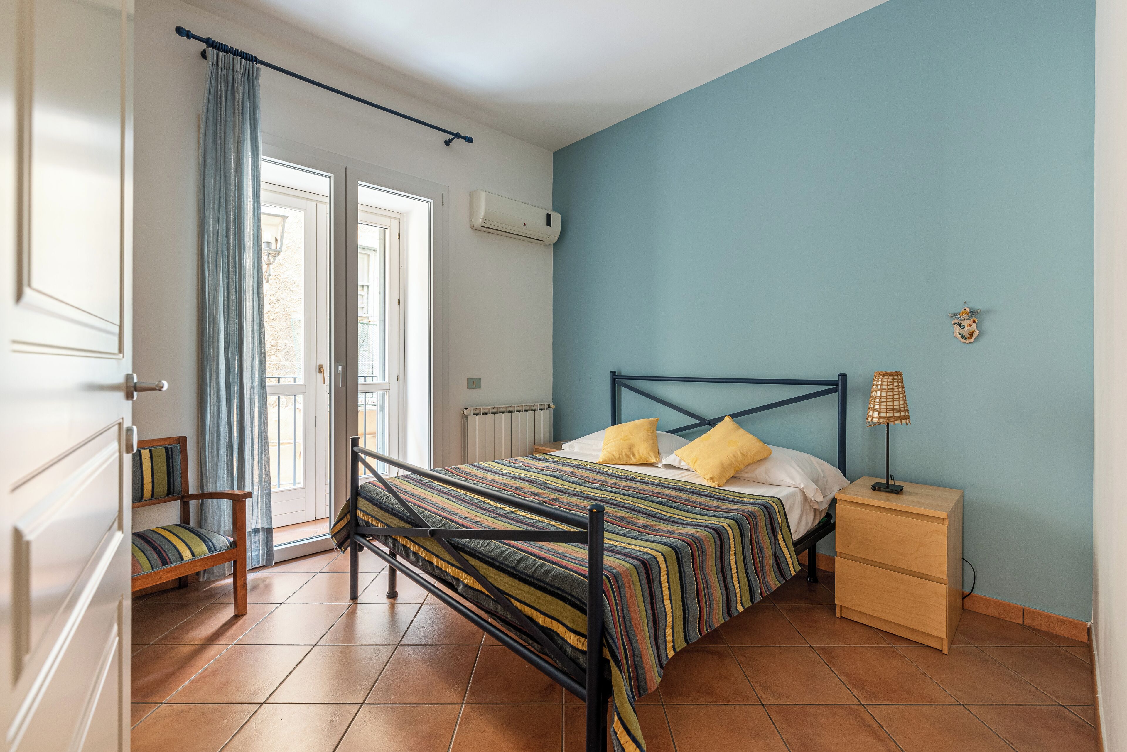 A bedroom with a bed, a nightstand, a chair, and a window with curtains.