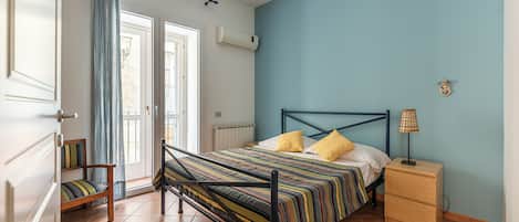 A bedroom with a bed, a nightstand, a chair, and a window with curtains.