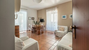 A spacious living room with a round wooden table, clear plastic chairs, a white sofa, and a white armchair. - Una Finestra sul Teatro Massimo by Wonderful Italy (Palermo)