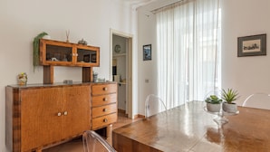 A dining area with a wooden table, chairs, a cabinet with glass doors, and a window with curtains. - Una Finestra sul Teatro Massimo by Wonderful Italy (Palermo)