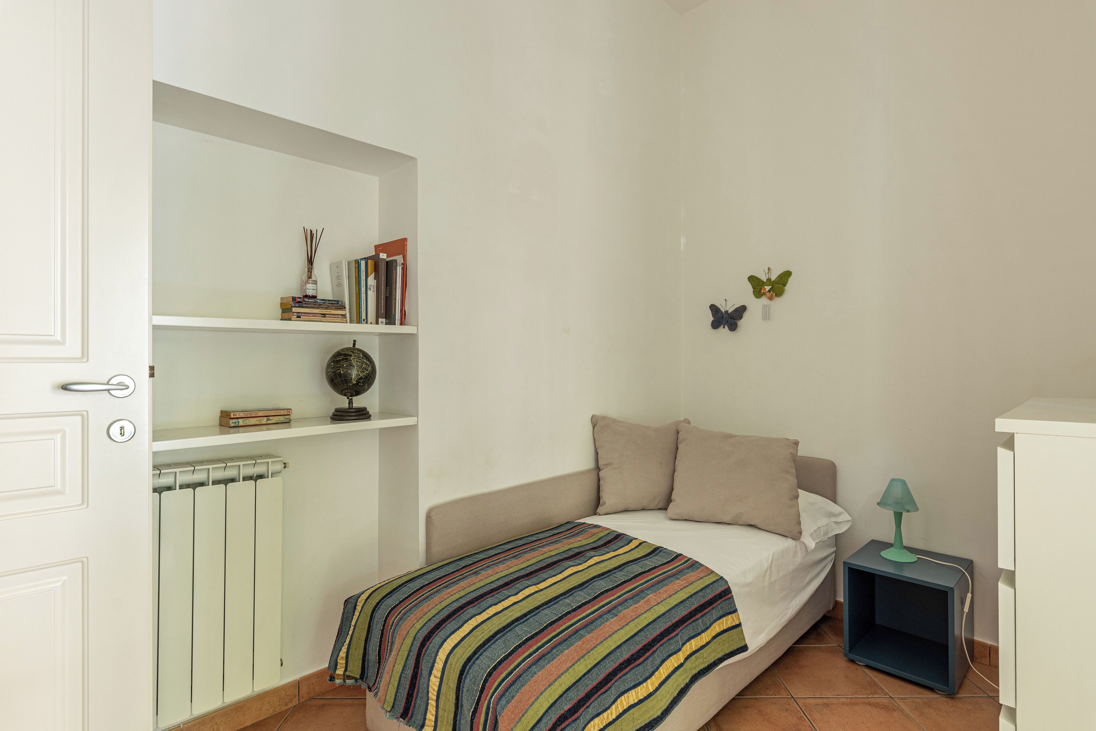 A bedroom with a bed, a bookshelf, a radiator, and a nightstand with a lamp.