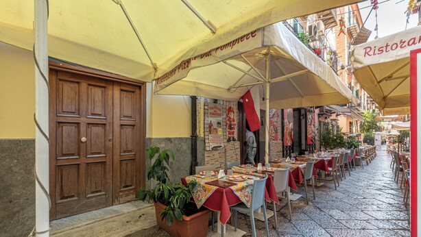 An outdoor dining area with tables and chairs under umbrellas, a wooden door, and a potted plant. - Una Finestra sul Teatro Massimo by Wonderful Italy (Palermo)