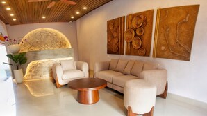 A modern living room with a stone wall, a beige sofa, a round coffee table, and a potted plant. - Maithala Villa (Kuta)