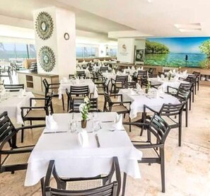 A restaurant with multiple tables set for dining, featuring a view of the sea. - Luxurious 3-bedroom Apartment With Shared Pool in Bolívar (Cartagena)