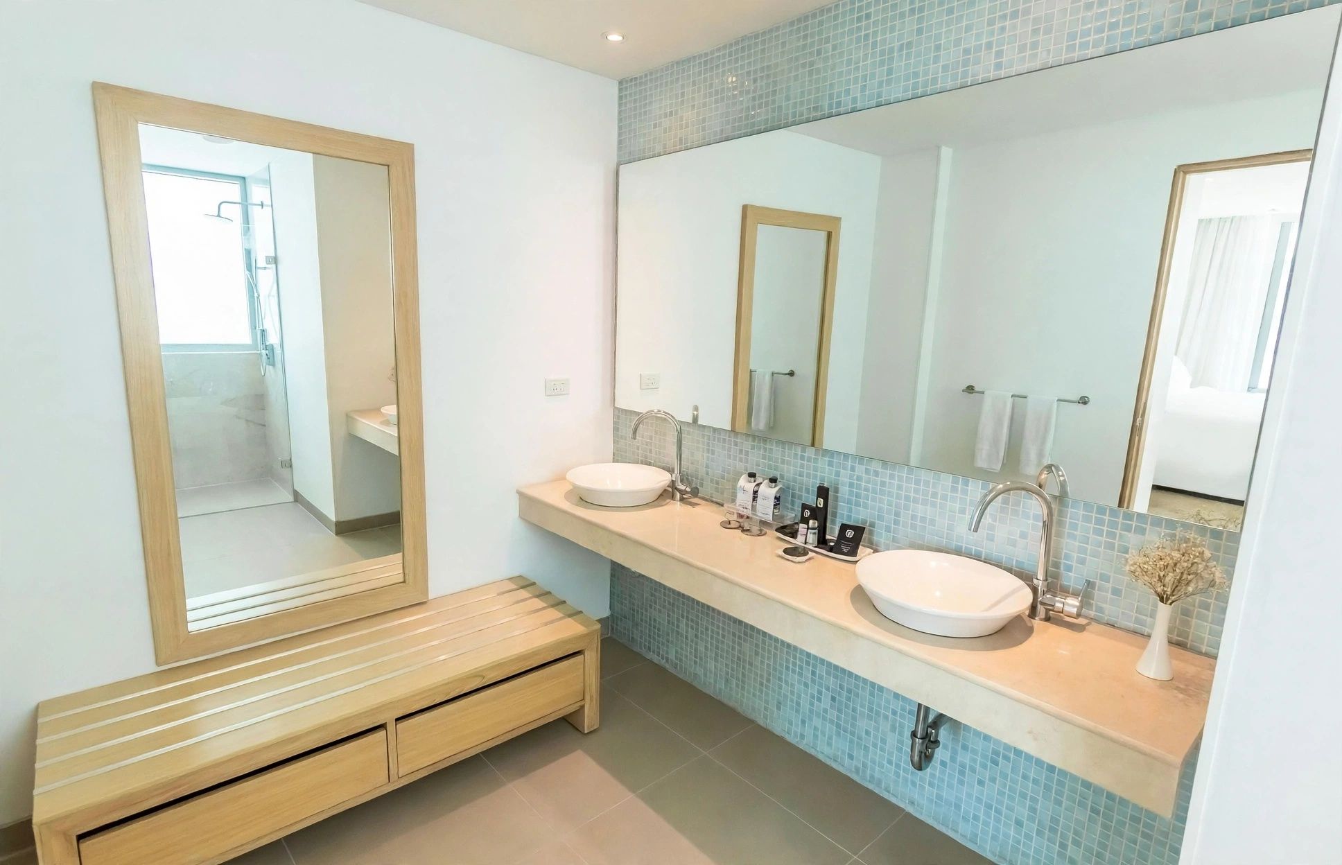 Une salle de bain moderne avec deux lavabos, un grand miroir et un banc en bois.