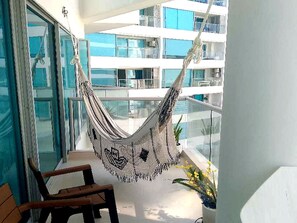 Un balcón con una hamaca, una silla y vista a un edificio de varios pisos.