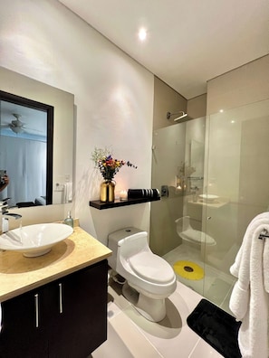 A modern bathroom with a large mirror, a white sink, a toilet, and a glass-enclosed shower area. - Beachfront 3-bedroom Apartment, 5 min to Airport (Cartagena)