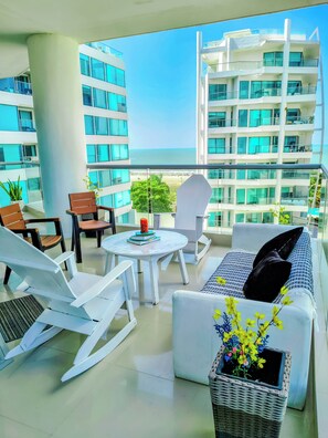 Un balcon avec un canapé blanc, des chaises, une petite table et une plante en pot.