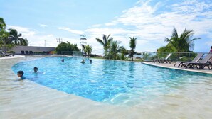 En swimmingpool med krystalklart vand, omgivet af palmer og liggestole.