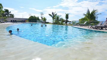 Una piscina con agua cristalina, rodeada de palmeras y sillas de descanso.
