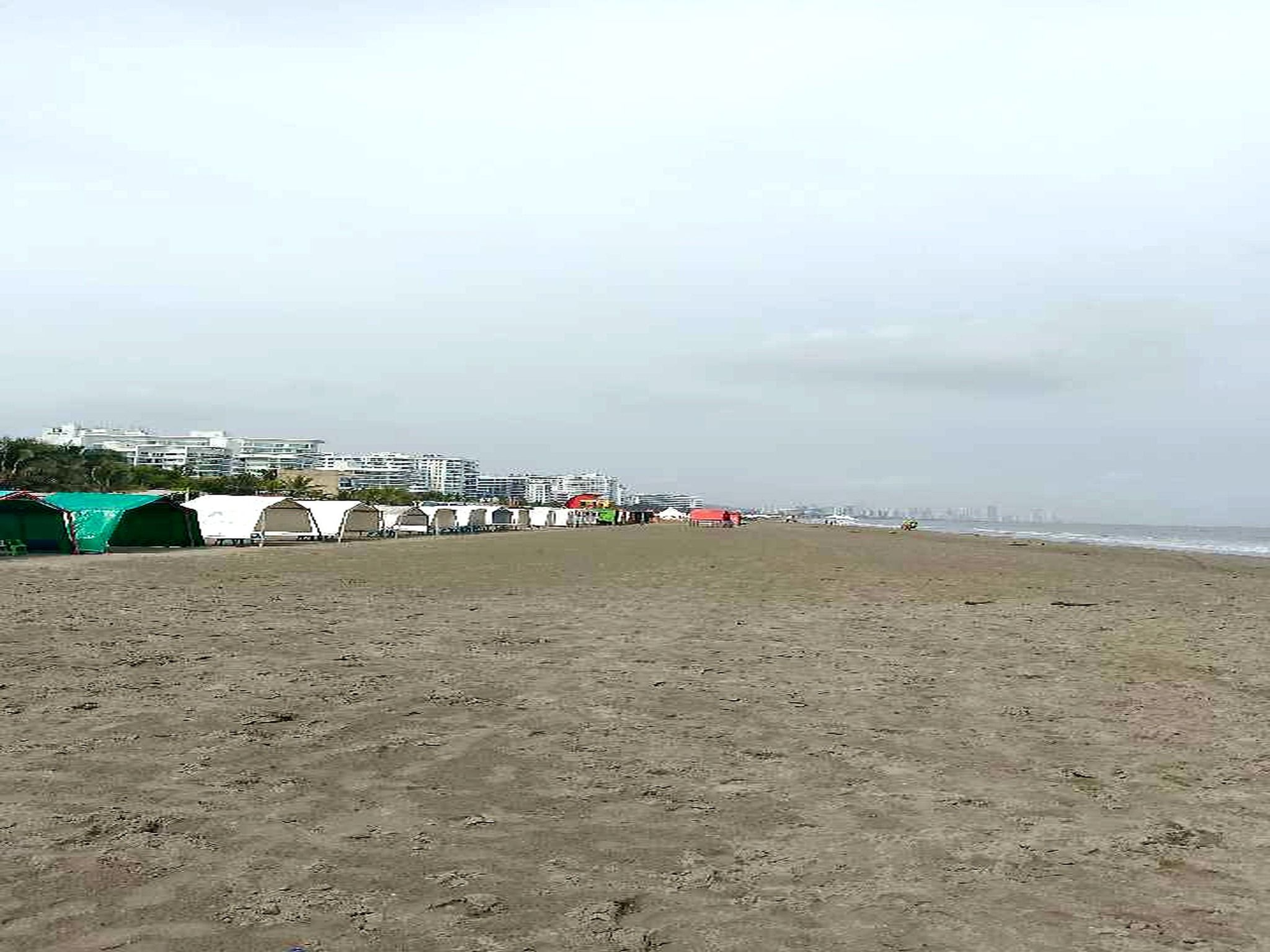 Una playa arenosa con tiendas de campaña y una hilera de edificios al fondo.