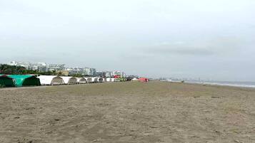 Una playa arenosa con tiendas de campaña y una hilera de edificios al fondo.