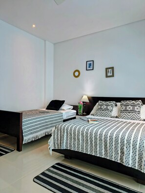 A bedroom with two beds, a nightstand with a lamp, a small table with a vase, and a wall-mounted picture. - Luxurious 3-bedroom Apartment With Shared Pool in Bolívar (Cartagena)