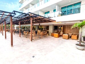 A covered outdoor seating area with tables and chairs, a bar area with seating, and a large potted plant. - Luxurious 3-bedroom Apartment With Shared Pool in Bolívar (Cartagena)