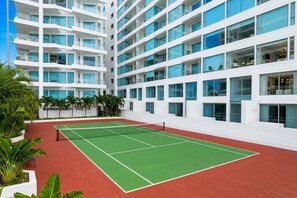 Un court de tennis jouxtant un bâtiment moderne doté de nombreux balcons et de grandes fenêtres.