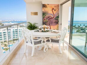 A balcony with a dining table, chairs, a potted plant, and a painting of a flamingo. - Luxurious 3-bedroom Apartment With Shared Pool in Bolívar (Cartagena)