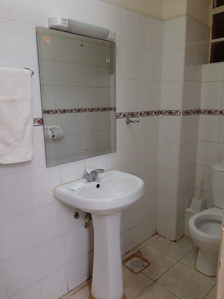 Casa de banho com lavatório branco, espelho e sanita.