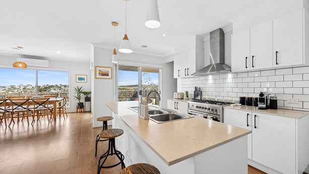 Une cuisine moderne avec des meubles blancs, une cuisinière en acier inoxydable et un grand îlot central doté de tabourets de bar.