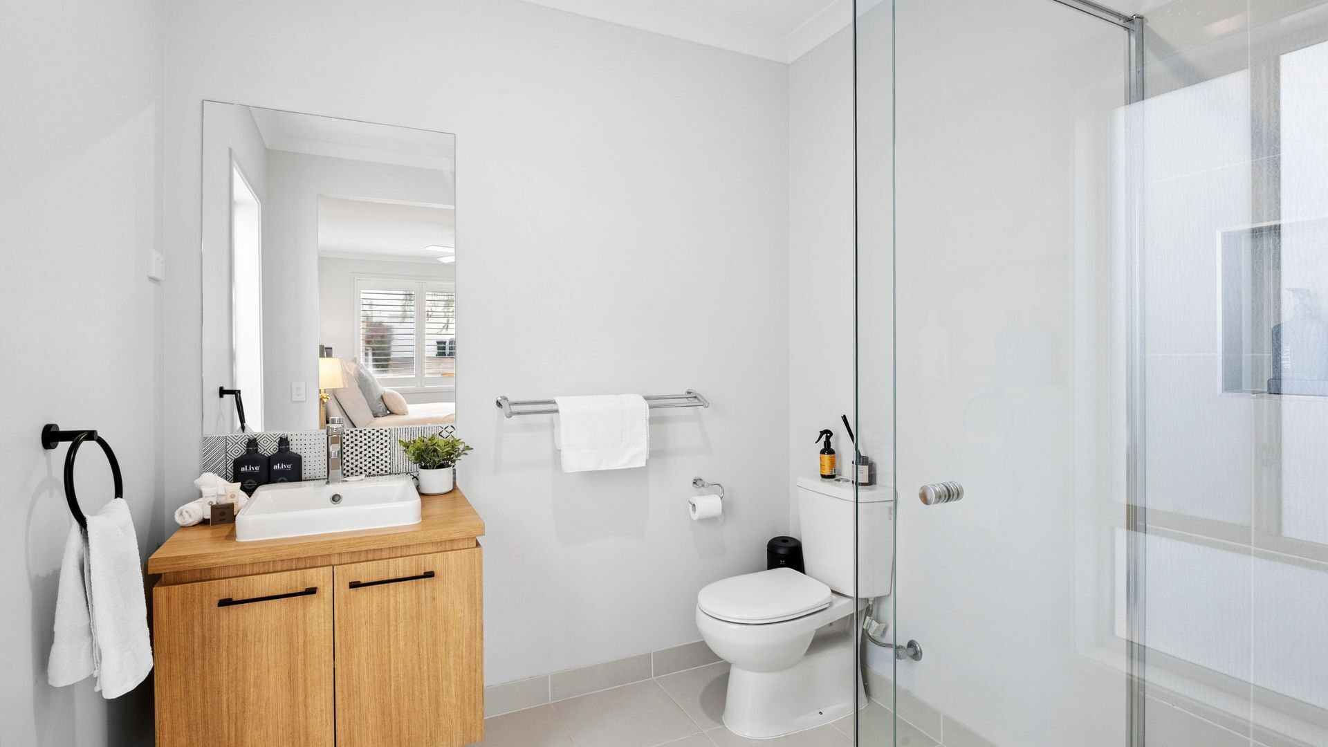 Ein modernes Badezimmer mit einem Holzlagerflächenschrank, einem großen Spiegel, einer Toilette und einer Duschkabine aus Glas.