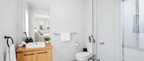 Ein modernes Badezimmer mit einem Holzlagerflächenschrank, einem großen Spiegel, einer Toilette und einer Duschkabine aus Glas.