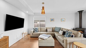 Un salon moderne avec un canapé d’angle, un téléviseur à écran plat, une cheminée et un plancher en bois.