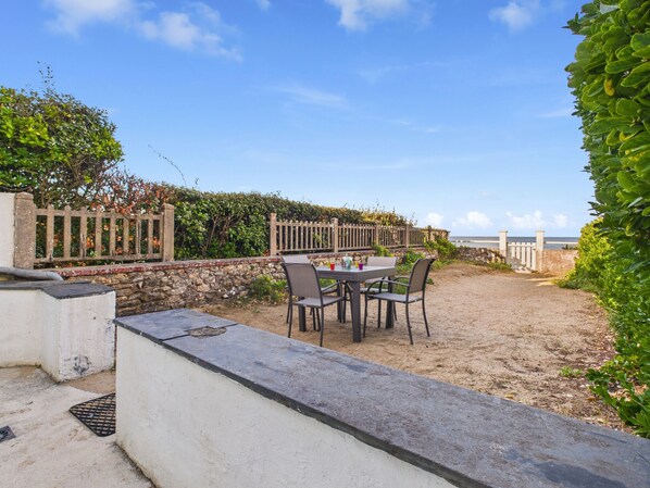 En patio med et bord og stole, en stenvæg, et træhegn og havudsigt.