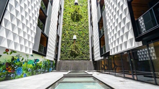 Un bâtiment moderne aux murs ornés de motifs géométriques, doté d’un élément aquatique central et d’un jardin vertical verdoyant.