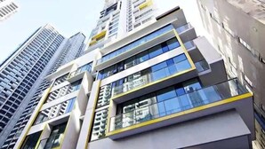 Un moderno edificio de gran altura con varios pisos, ventanas amplias y un detalle amarillo en la fachada.