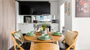 A modern kitchen with white cabinets, a black TV, and a dining area with green plates and wooden chairs. - A Cozy 2BR Apt Next to Southern Cross Free Parking (Melbourne)