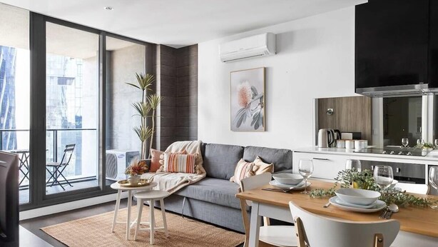 Eine moderne Küche mit Essbereich, großen Fenstern und einem grauen Sofa.