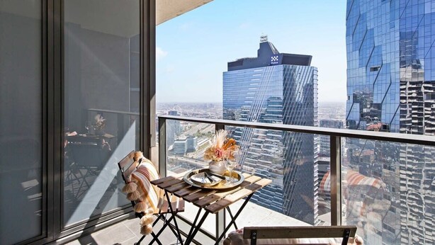 A balcony with a table set for two, overlooking a cityscape with modern buildings. - A Cozy 2BR Apt on Spencer St With Free Parking (Melbourne)