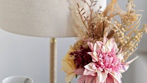 Une lampe avec un abat-jour beige, une tasse blanche et un vase contenant des fleurs et des plantes séchées.