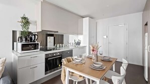Une cuisine moderne avec des meubles blancs, une table à manger dressée avec des assiettes et des verres, et une plante suspendue.