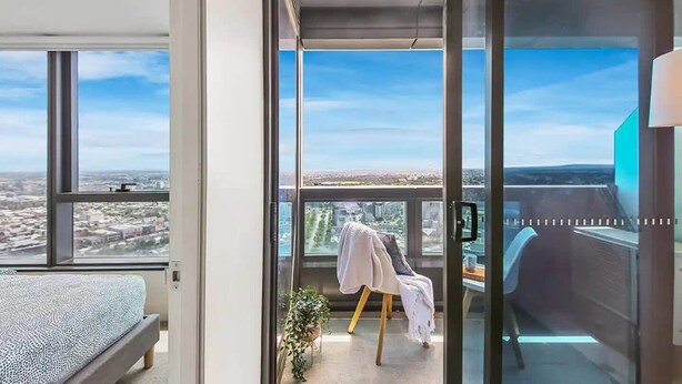 A modern bedroom with a large window, a bed, a chair, and a small table with a plant. - A Cozy & Modern 2BR Apartment, Fantastic Views (Melbourne)