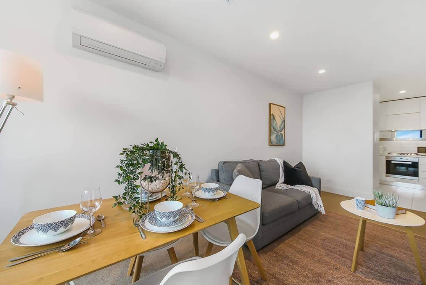 A modern living room with a dining area, grey sofa, and a small kitchen.