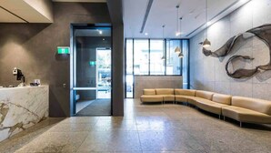 A modern lobby with a marble reception desk, a curved beige sofa, and a large abstract wall art piece. - A Cozy & Modern 2BR Apartment, Fantastic Views (Melbourne)